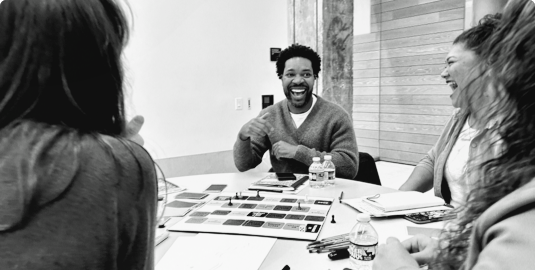A Black man and Asian American woman sit and laugh during a group discussion with two other people.